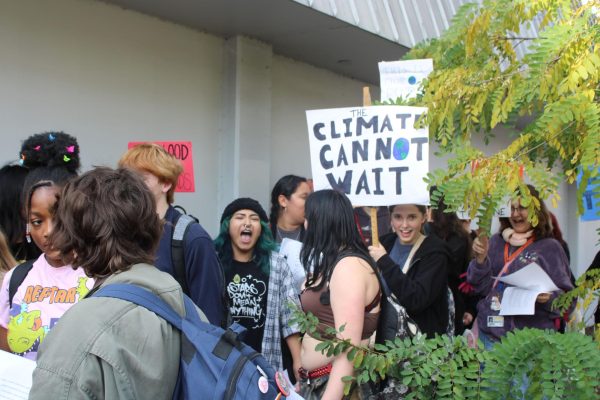 Students chant and march across the street from Benson, while holding signs including one that says "Climate Cannot Wait."