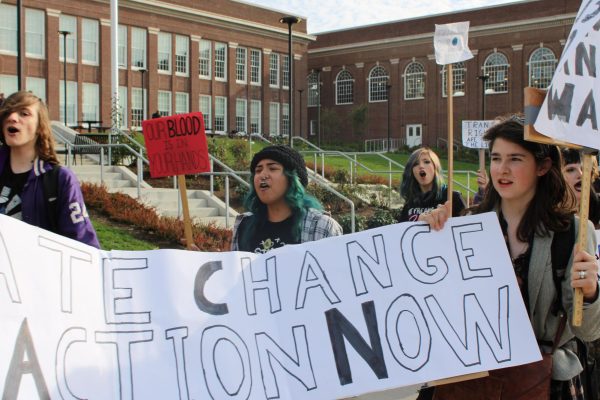 Students chant and march across the street from Benson, while holding signs including one that says "Climate Cannot Wait."